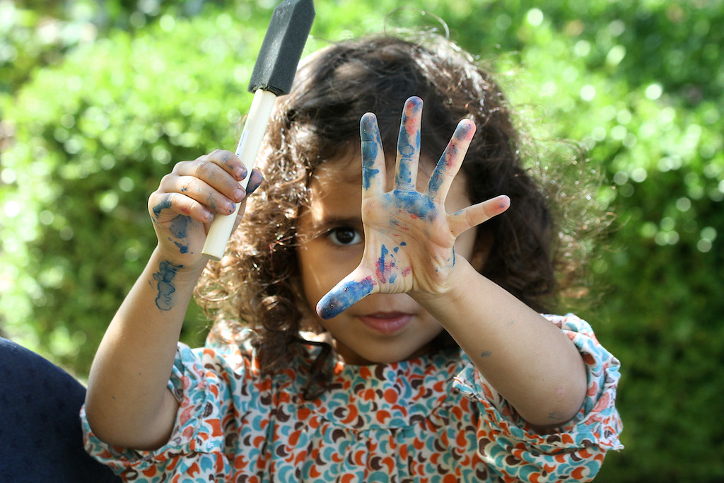 Child with hand out covered in arts and crafts paint